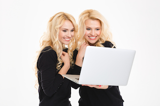 portrait of a pretty sisters twins using laptop computer isolated on a white background